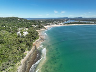 Aerial view of Noosa with rocky national park coastline in the foreground and Noosa Main Beach and township behind.